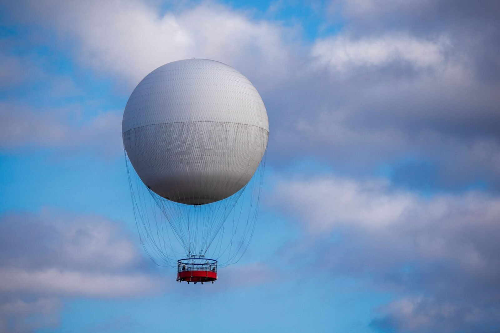 A white hot air balloon soaring in a clear blue sky with fluffy clouds.