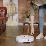 A woman in jeans interacts with a robotic vacuum cleaner in a cozy, stylish living room.
