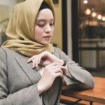 A young woman in a beige hijab looking at her smartwatch indoors.