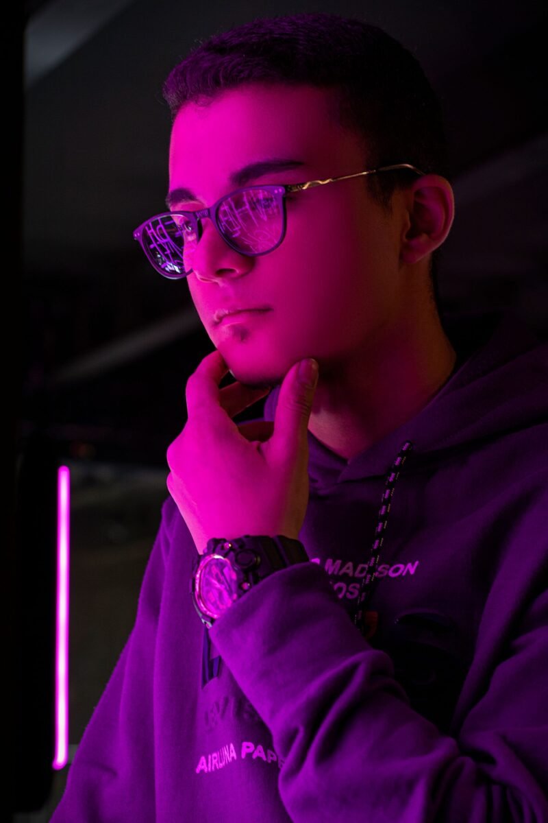 Portrait of a young man with eyeglasses posing indoors under vibrant neon pink lighting.