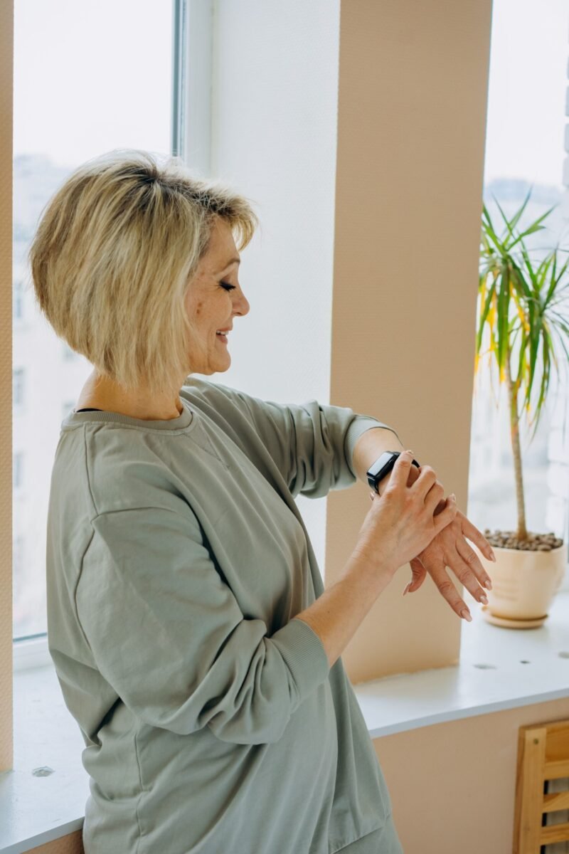 Elderly woman smiling while checking her smartwatch indoors by a window.