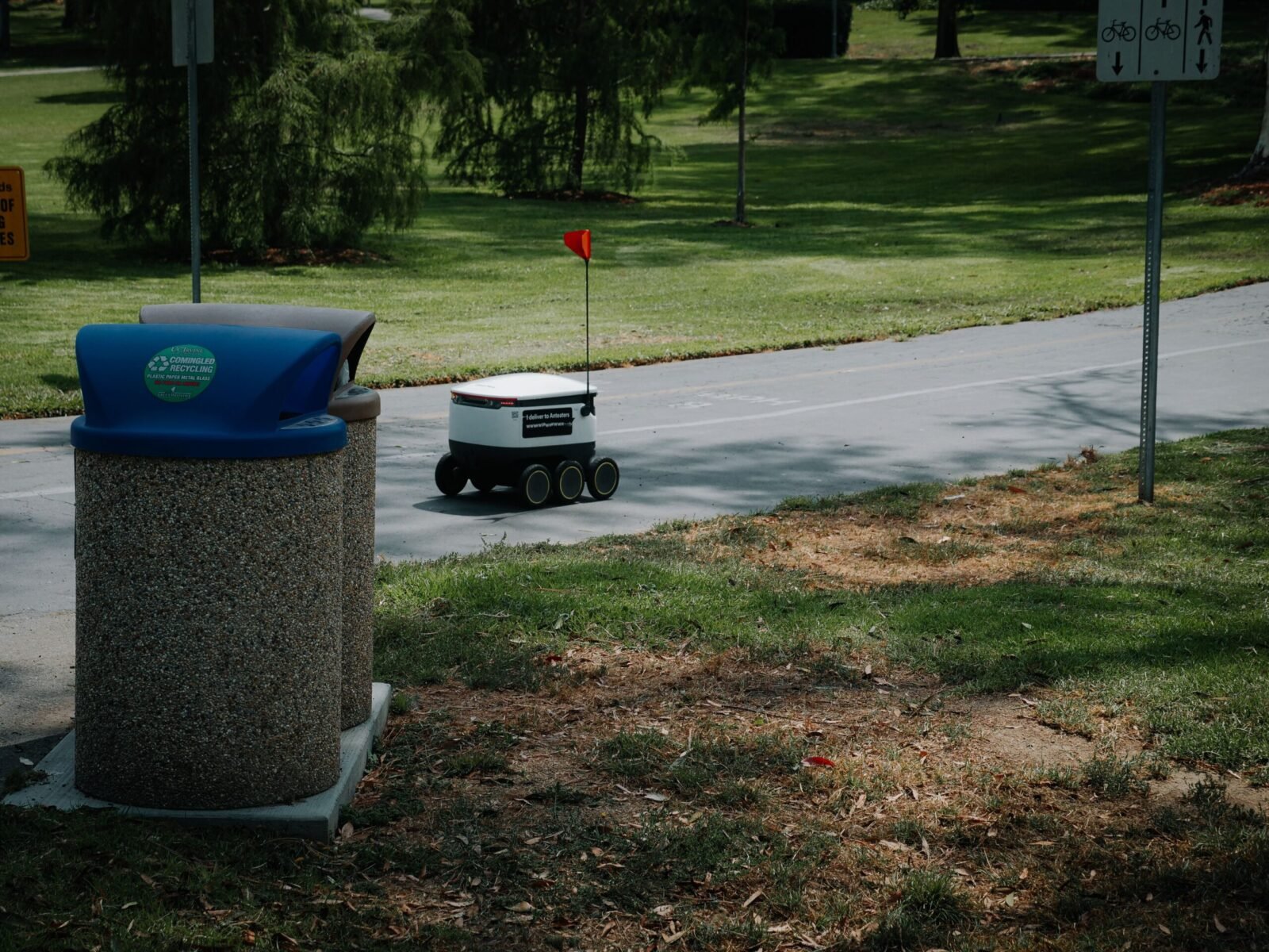 Autonomous delivery robot on a park pathway, showcasing modern technology in a natural outdoor setting.